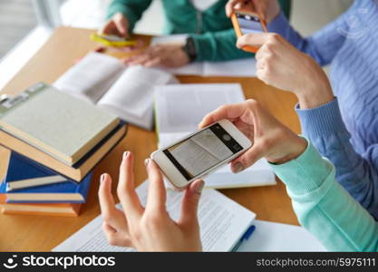 people, education, technology and exam concept - close up of students with smartphones taking picture of books page and making cheat sheet in school library