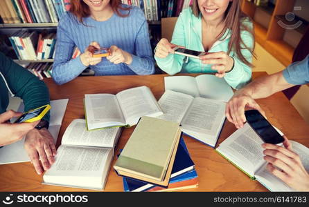 people, education, technology and exam concept - close up of students with smartphones taking picture of books page and making cheat sheet in school library