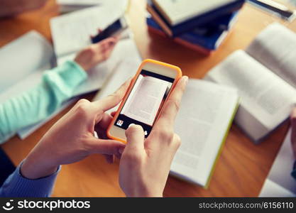 people, education, technology and exam concept - close up of students with smartphones taking picture of books page and making cheat sheet in school library