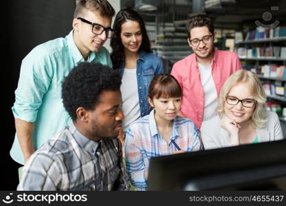 people, education, technology and school concept - group of happy smiling international students with computers at library in university