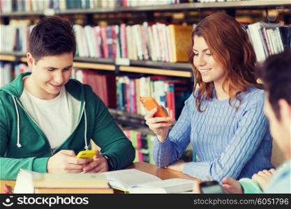 people, education, technology and school concept - group of happy students with smartphones and books texting message or networking in library