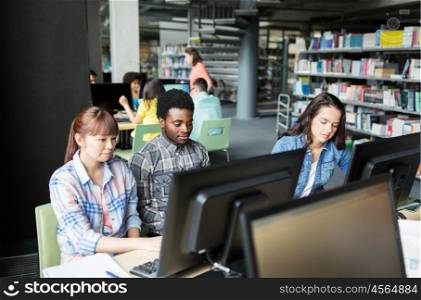 people, education, technology and school concept - group of international students with computers at library in university