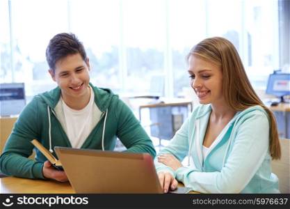people, education, technology and school concept - happy students with laptop computer and books in library