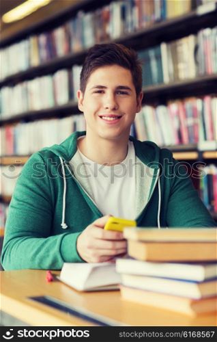 people, education, technology and school concept - male student with smartphone and books in library