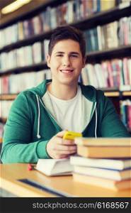 people, education, technology and school concept - male student with smartphone and books in library