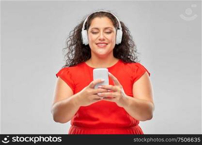 people, electronics and technology concept - happy woman in wireless headphones listening to music on smartphone over grey background. woman in headphones listens to music on smartphone