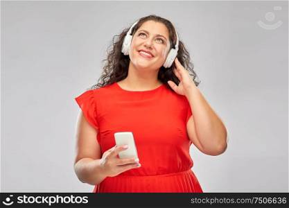 people, electronics and technology concept - happy woman in wireless headphones listening to music on smartphone over grey background. woman in headphones listens to music on smartphone