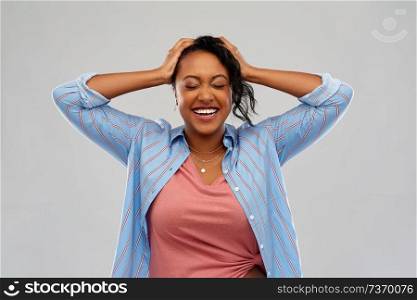 people, emotion and expression concept - happy african american young woman holding to her head over grey background. happy african american woman holding to her head