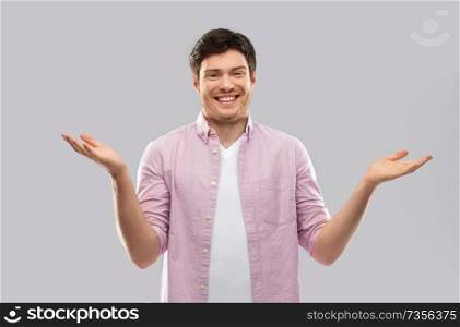 people, emotion and expression concept - happy young man shrugging over grey background. happy young man shrugging over grey background