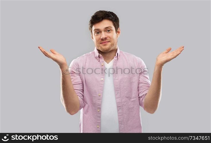 people, emotion and expression concept - young man shrugging over grey background. young man shrugging over grey background