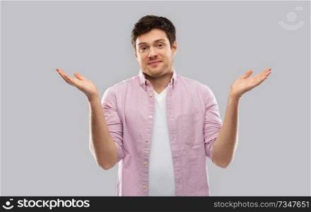 people, emotion and expression concept - young man shrugging over grey background. young man shrugging over grey background