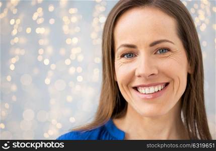 people, emotion and facial expression concept - face of happy smiling middle aged woman over lights background. face of smiling middle aged woman over lights