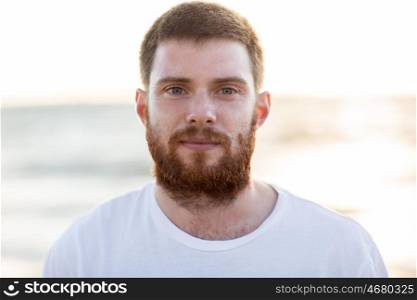 people, emotion and facial expression concept - face of happy smiling young man with red beard on beach