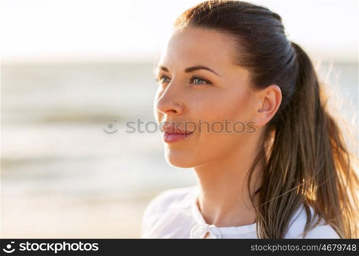 people, emotion and facial expression concept - face of happy smiling young woman on beach