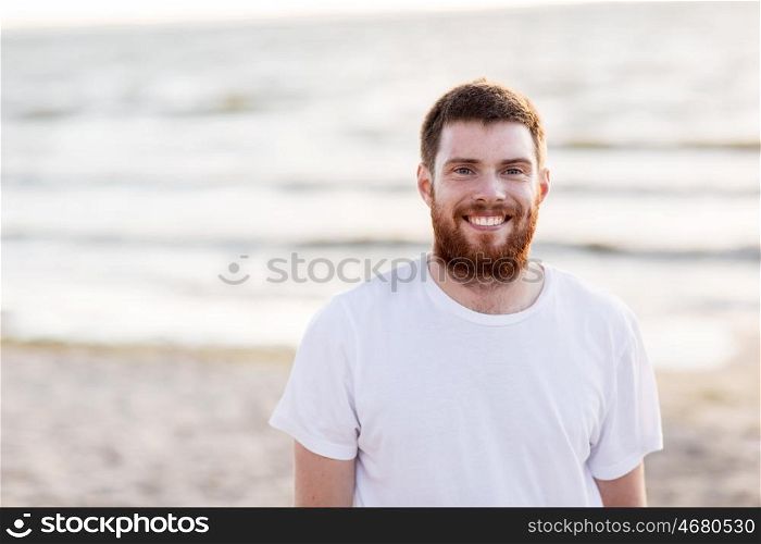people, emotion and facial expression concept - happy smiling young man with red beard on beach