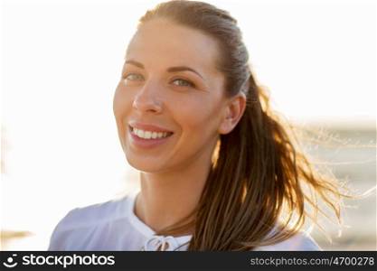people, emotion and facial expression concept - happy smiling young woman face outdoors over sunlight