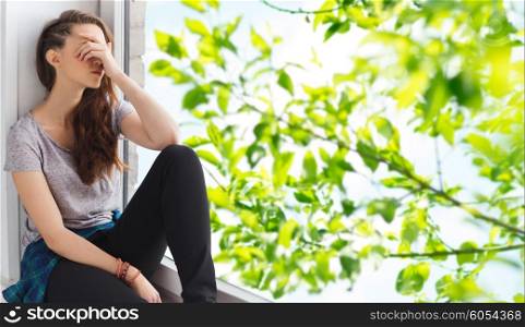 people, emotion and teens concept - sad unhappy pretty teenage girl sitting on windowsill over summer tree brunch background