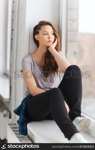 people, emotion and teens concept - sad unhappy pretty teenage girl sitting on windowsill