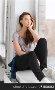 people, emotion and teens concept - sad unhappy pretty teenage girl sitting on windowsill