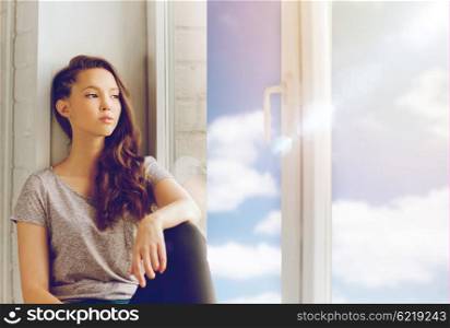 people, emotion and teens concept - sad unhappy pretty teenage girl sitting on windowsill
