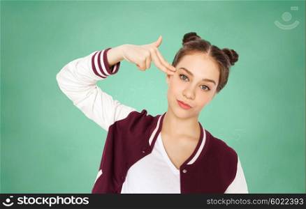people, emotion, education, stress and teens concept - bored teenage student girl making headshot by finger gun gesture over green school chalk board background