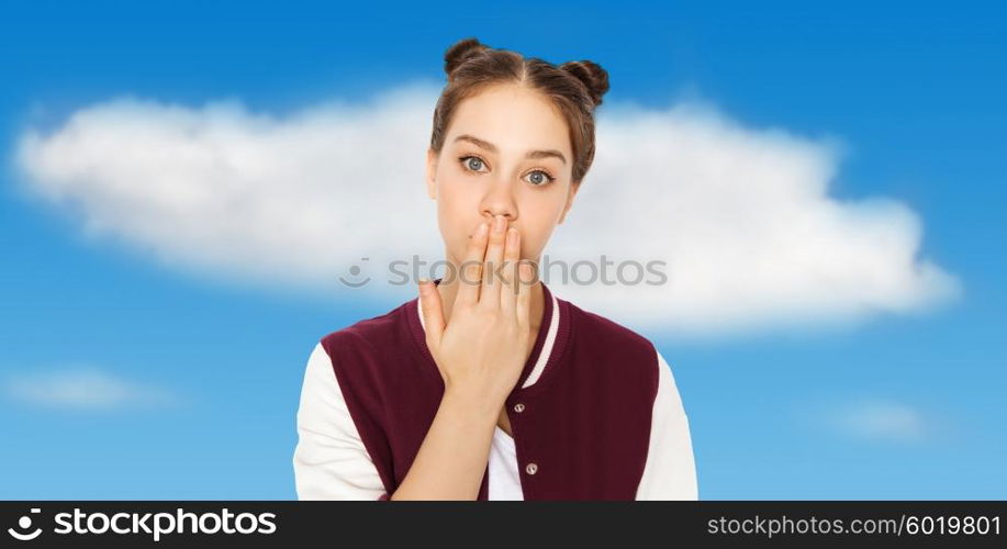 people, emotion, expression and teens concept - confused teenage girl covering her mouth by hand over blue sky and clouds background