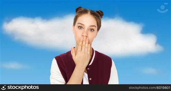 people, emotion, expression and teens concept - confused teenage girl covering her mouth by hand over blue sky and clouds background