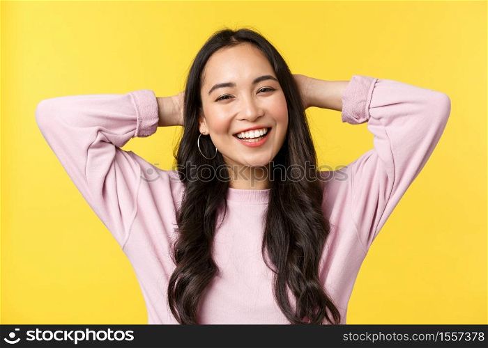People emotions, lifestyle leisure and beauty concept. Carefree cheerful asian girl smiling broadly, holding hands behind head, enjoying summer weekends, standing yellow background.. People emotions, lifestyle leisure and beauty concept. Carefree cheerful asian girl smiling broadly, holding hands behind head, enjoying summer weekends, standing yellow background
