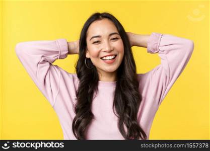 People emotions, lifestyle leisure and beauty concept. Carefree cheerful asian girl smiling broadly, holding hands behind head, enjoying summer weekends, standing yellow background.. People emotions, lifestyle leisure and beauty concept. Carefree cheerful asian girl smiling broadly, holding hands behind head, enjoying summer weekends, standing yellow background