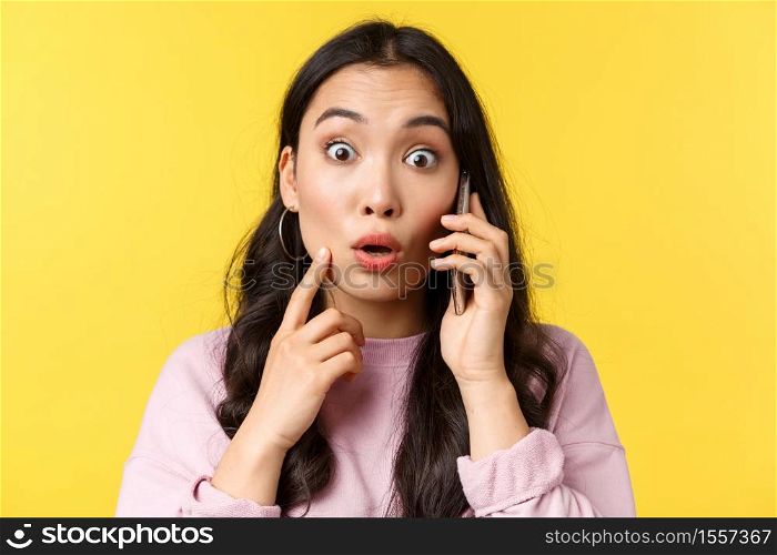 People emotions, lifestyle leisure and beauty concept. Close-up of shocked and surprised asian girl talking on phone, stare camera with popped eyes as hear big news, yellow background.. People emotions, lifestyle leisure and beauty concept. Close-up of shocked and surprised asian girl talking on phone, stare camera with popped eyes as hear big news, yellow background