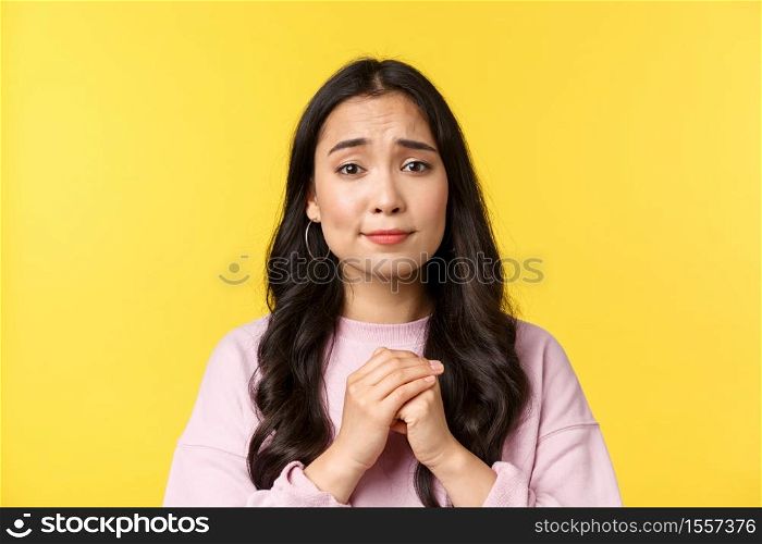 People emotions, lifestyle leisure and beauty concept. Close-up of silly hopeful asian girl pleading or apologizing, holding hands in pray and looking pitiful, yellow background.. People emotions, lifestyle leisure and beauty concept. Close-up of silly hopeful asian girl pleading or apologizing, holding hands in pray and looking pitiful, yellow background