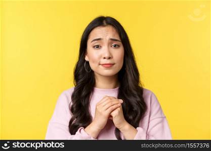 People emotions, lifestyle leisure and beauty concept. Close-up of silly hopeful asian girl pleading or apologizing, holding hands in pray and looking pitiful, yellow background.. People emotions, lifestyle leisure and beauty concept. Close-up of silly hopeful asian girl pleading or apologizing, holding hands in pray and looking pitiful, yellow background
