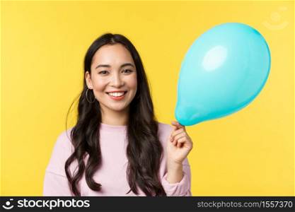 People emotions, lifestyle leisure and beauty concept. Cute smiling asian girl holding blue balloon as congratulating with big event, standing yellow background, through up surprise party.. People emotions, lifestyle leisure and beauty concept. Cute smiling asian girl holding blue balloon as congratulating with big event, standing yellow background, through up surprise party