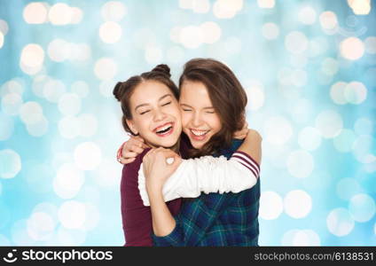 people, emotions, teens and friendship concept - happy smiling pretty teenage girls hugging and laughing over blue holidays lights background