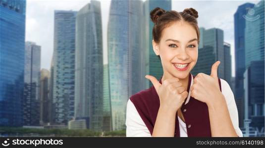 people, emotions, travel, gesture and teens concept - happy smiling pretty teenage girl showing thumbs up over singapore city skyscrapers background