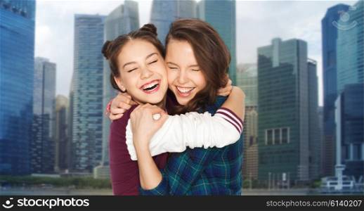 people, emotions, travel, tourism and friendship concept - happy smiling pretty teenage girls hugging and laughing over singapore city skyscrapers background