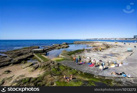 People enjoying the sun and the Atlantic Ocean around a swimming pool built on the on the rocks of the Tamariz Beach, in Estoril, Portugal