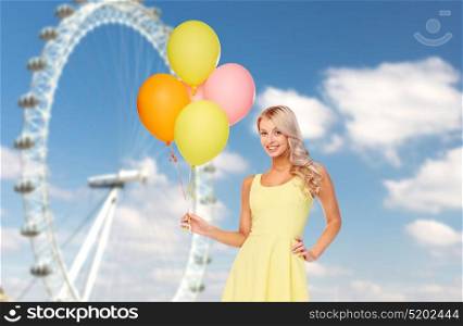 people, entertainment and summer concept - happy young woman or teen girl in yellow dress with helium air balloons over ferris wheel and sky background. happy woman with air balloons over ferris wheel