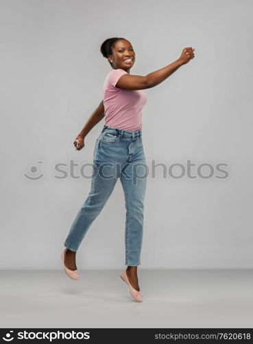 people, ethnicity and portrait concept - happy african american young woman jumping or running over grey background. happy african american woman jumping over grey