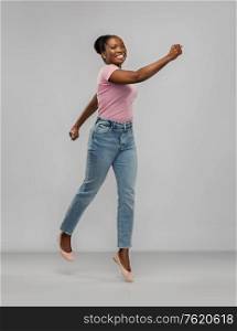 people, ethnicity and portrait concept - happy african american young woman jumping or running over grey background. happy african american woman jumping over grey