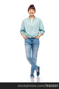 people, ethnicity and portrait concept - happy asian young woman in cotton shirt and jeans over white background. happy asian woman over white background