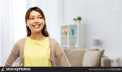 people, ethnicity and portrait concept - happy asian young woman looking up over home room background. happy asian woman looking up at home
