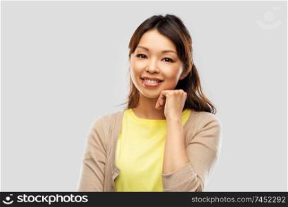 people, ethnicity and portrait concept - happy asian young woman over grey background. happy asian woman over grey background