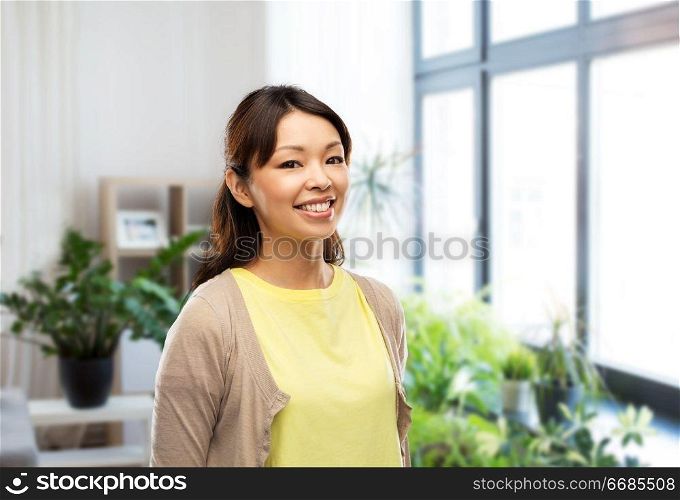 people, ethnicity and portrait concept - happy asian young woman over home background. happy asian woman over home background