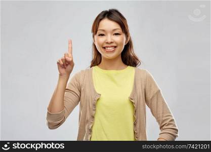 people, ethnicity and portrait concept - happy asian young woman pointing finger up over grey background. happy asian woman pointing finger up