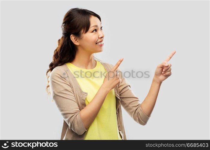 people, ethnicity and portrait concept - happy asian young woman pointing fingers up over grey background. happy asian woman pointing fingers up