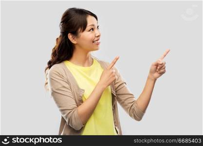 people, ethnicity and portrait concept - happy asian young woman pointing fingers up over grey background. happy asian woman pointing fingers up