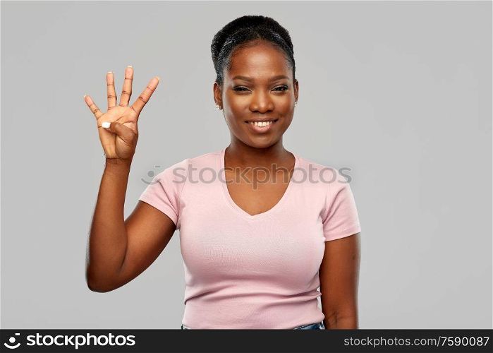 people, ethnicity and portrait concept - happy smiling african american young woman showing four fingers over grey background. happy african american woman showing four fingers