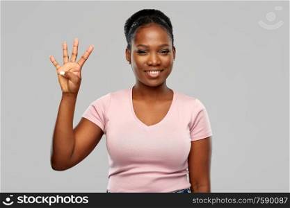 people, ethnicity and portrait concept - happy smiling african american young woman showing four fingers over grey background. happy african american woman showing four fingers