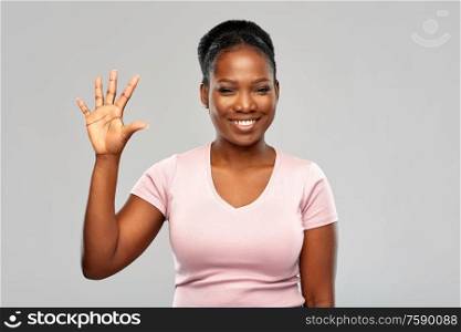 people, ethnicity and portrait concept - happy smiling african american young woman showing five fingers over grey background. happy african american woman showing five fingers